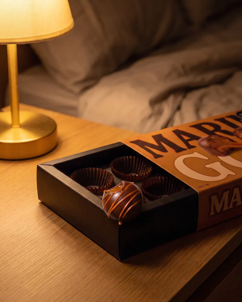 Caja Manjar de olla abierta sobre una mesa de noche, a la luz de una lámpara, con dos pirotines vacíos y un bombón mordido