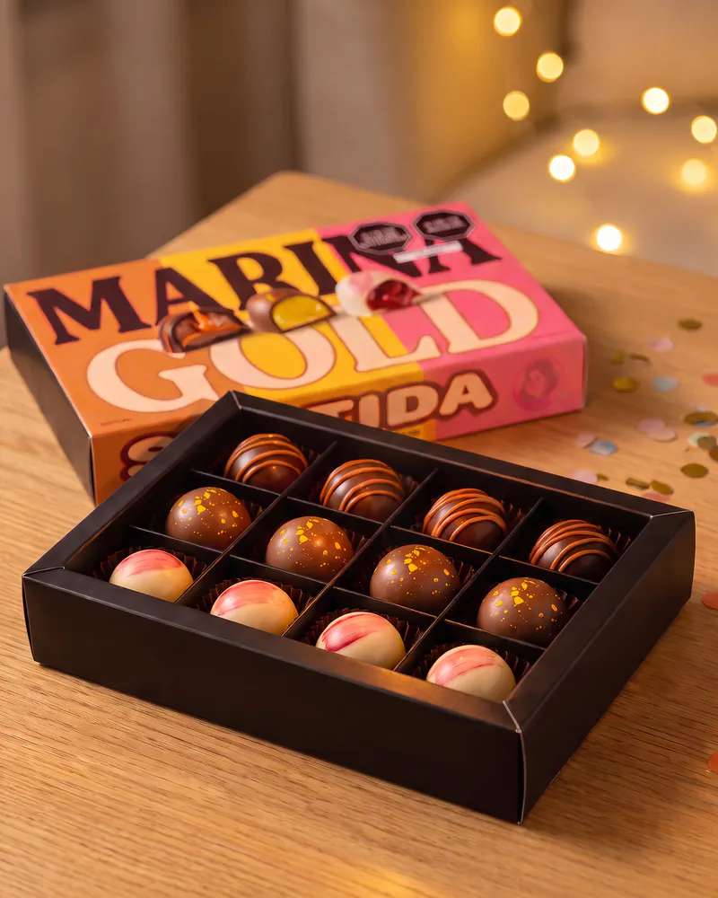 Caja de bombones abierta junto a la caja Surtida, con luces cálidas y confeti de celebración